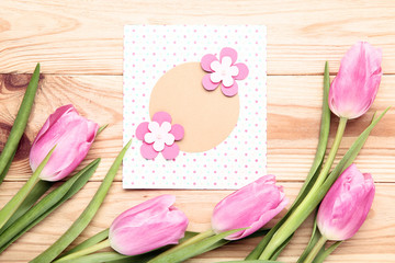 Greeting card with pink tulip flowers on wooden table