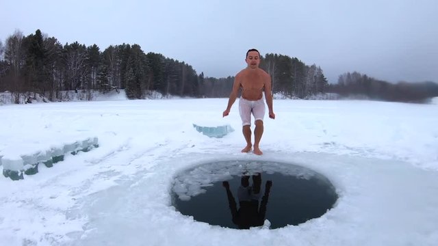 Young man jumps into the ice hole and haves recreational winter swim with joy