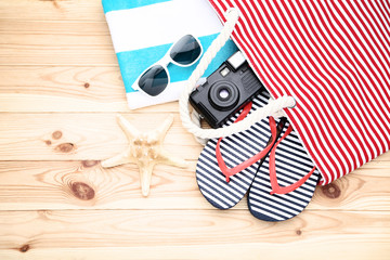 Summer bag with flip flops and retro camera on wooden table