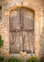 Fototapeta na wymiar Stone in heart shape lying before old weathered doors in old brick wall on the island Kythira, Greece, alle in yellow and brown color