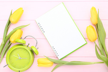 Yellow tulips with alarm clock and blank notepad on wooden table