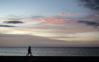 Silhouettes of the Couple of kids walking at the seafront during sunset