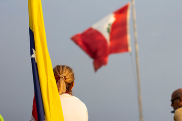 Blonde woman looking at Peruvian flag while holding Venezuelan flag at protest against Nicolas Maduro