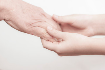 the hands of an old man and a child holding each other on a white background. contrast. idea