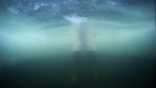 Young man haves recreational winter swim. Underwater blurred view