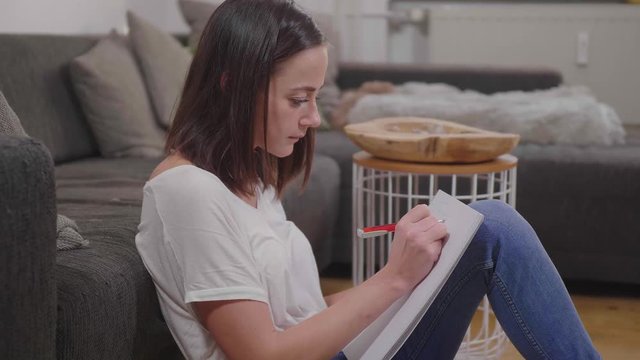 Young woman sits on the floor and writes some notes in her college block