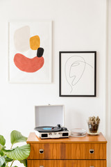 Vintage and retro interior of living room with design commode, vinyl recorder, cacti and mock up posters frames on the white walls. Cozy room with brown wooden parquet and plants.