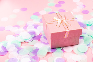 Present box on pink background with multicolored confetti.