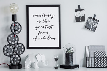 Modern and stylish black and white home decor mock up. Creative desk with blank picture frame or poster, desk objects, office supplies, elephant figure and design table lamp on a white background.
