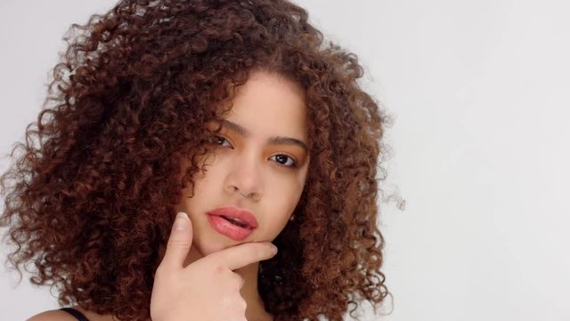 mixed race black woman with freckles and curly hair in studio on white poses to a camera touches her ideal skin and watching to the camera.