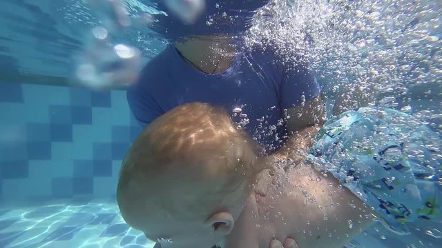 Happy smiling toddler is diving under water with father
