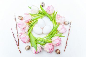Spring greeting card. Easter eggs in nest and pink fresh tulip flowers bouquet on rustic white wooden background. Easter concept. Flat lay top view copy space. Spring flowers tulips