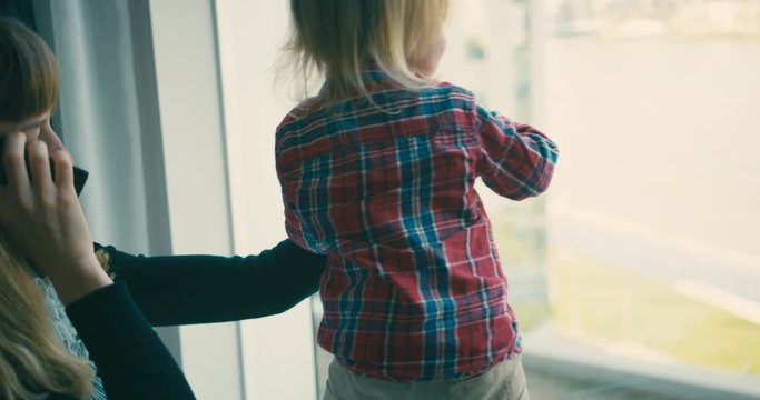 Young mother on the phone whil eplaying with toddler by city window