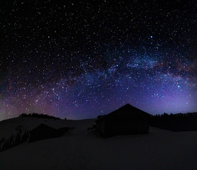 A charming moonlit night in the Ukrainian Carpathian Mountains with the moonlight and millions of stars and galaxies with winter snowy landscapes and houses on the valleys.