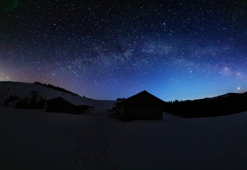 A charming moonlit night in the Ukrainian Carpathian Mountains with the moonlight and millions of stars and galaxies with winter snowy landscapes and houses on the valleys.