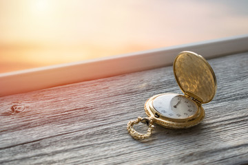 Gold Vintage pocket watch with sunset light on wooden background. Hourglass or sand timer, symbol...
