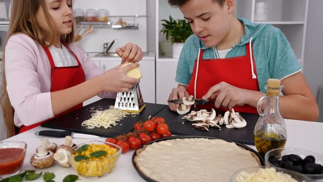 Teenagers making pizza in the kitchen at home - preparing the ingredients, camera tilt up