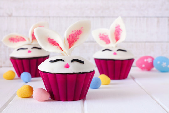 Easter bunny cupcakes, close up against a white wood background with candy eggs