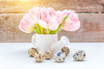 Spring greeting card. Easter eggs pink fresh tulip flowers bouquet small toy watering can vase on rustic shabby wooden background. Easter concept. Copy space. Spring flowers tulips