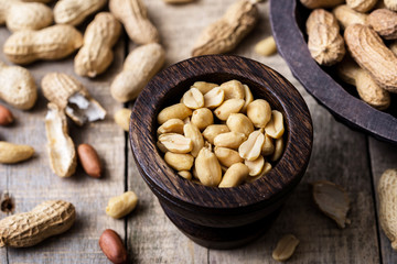 Peanuts in small dark wooden bowl on natural rustic desk.