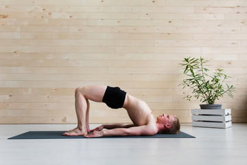 Sporty man practicing yoga on yoga class, bridgepose