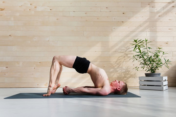 Sporty man practicing yoga on yoga class, bridgepose