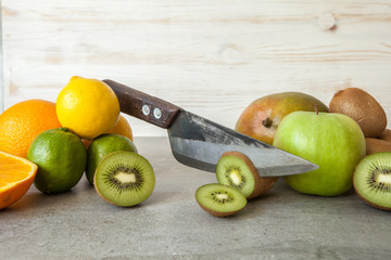 Fresh citrus fruits, half cut kiwi orange and lemons on cutting board with knife on stone background.