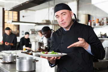 Positive male cook with cooked dish in restaurant kitchen