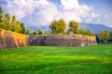Defensive brick city wall, grass green lawn, trees and Tuscany hills and mountains with beautiful...