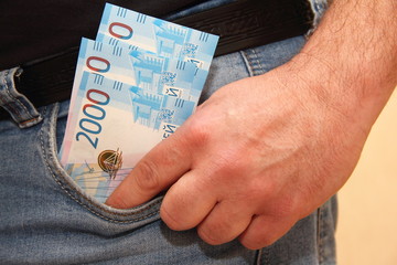 New banknotes 2000 Russian rubles in the pocket of men's jeans with hand - salary, subsistence