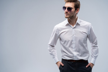 portrait of a young fashion man wearing sunglasses on grey background.