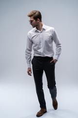 young man in sunglasses looks to side while walking on gray studio background.