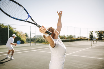 Senior woman making a serve while playing tennis