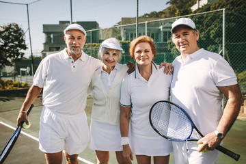 Senior men and women standing together on a tennis court