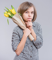 Beautiful Girl holding Bouquet of Tulips, on gray background. Thoughtful Teen Girl has prepared a Surprise for Mum - yellow Flowers. Funny Teenager dreams and looking away.