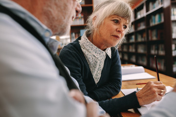 Senior couple sitting in library reading books