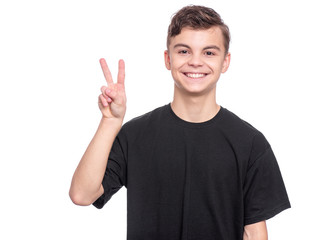 Handsome Teen Boy in black T-Shirt making Victory Gesture. Portrait of caucasian Smiling Teenager isolated on white background. Happy child looking at camera.
