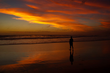 Young man walking outdoors watching the sunset at a beach. Thinking and relaxing concept.