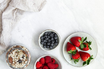 granola with bowl raspberries, strawberry, blueberry on marble textured background