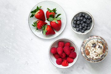 granola with bowl raspberries, strawberry, blueberry on marble textured background