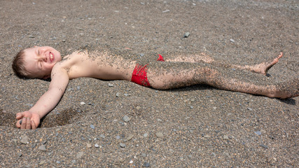 The boy lies on the beach and is covered with small pebbles. © Dmitrii Potashkin