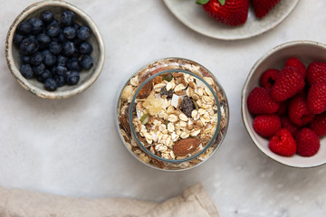 granola with bowl raspberries, strawberry, blueberry on marble textured background