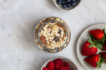 granola with bowl raspberries, strawberry, blueberry on marble textured background
