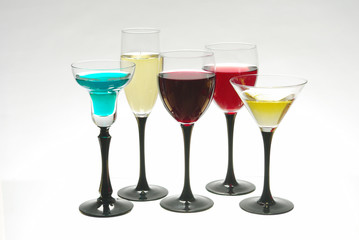 Five glasses with multi-colored cocktails on a light background.