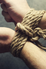 Male hands tied by a rough rope on a dark background close-up. Symbol of bondage, slavery