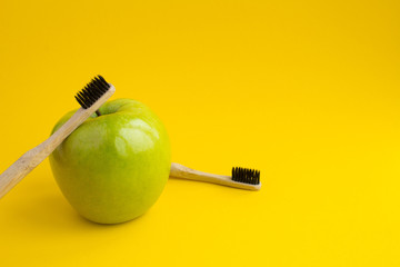 Two bamboo toothbrushes and green apple on the yellow background.Copy space.