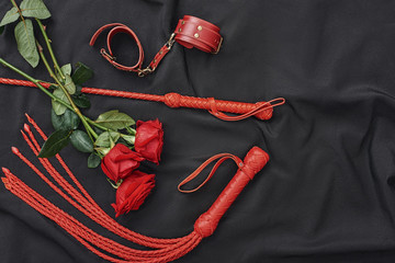 Love games. Top view of bdsm leather kit (handcuffs, whip) and beautiful red roses against of black...
