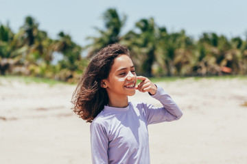 Portrait of little girl wearing sun protective clothing and applying sunscreen on the beach