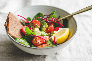 Vegetarian healthy salad is made from swiss chard leaves, cherry tomatoes, avocado, lemon juice and olive oil into a ceramic portion bowl.
