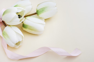 Beautiful fake white tulips with pink ribbon in pastel background. Concept for Mother's Day celebration with copy space.